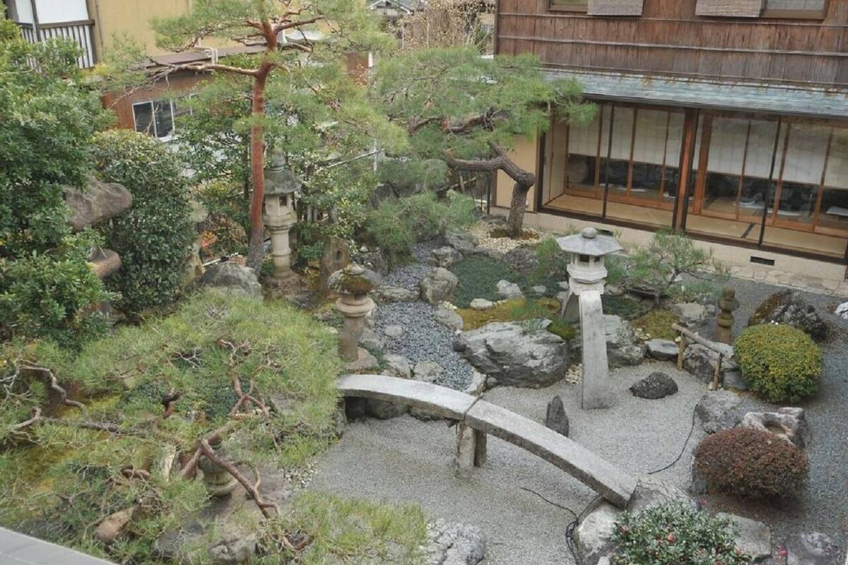 Un jardín japonés tradicional con un puente de piedra, rocas y una pequeña fuente de agua.
