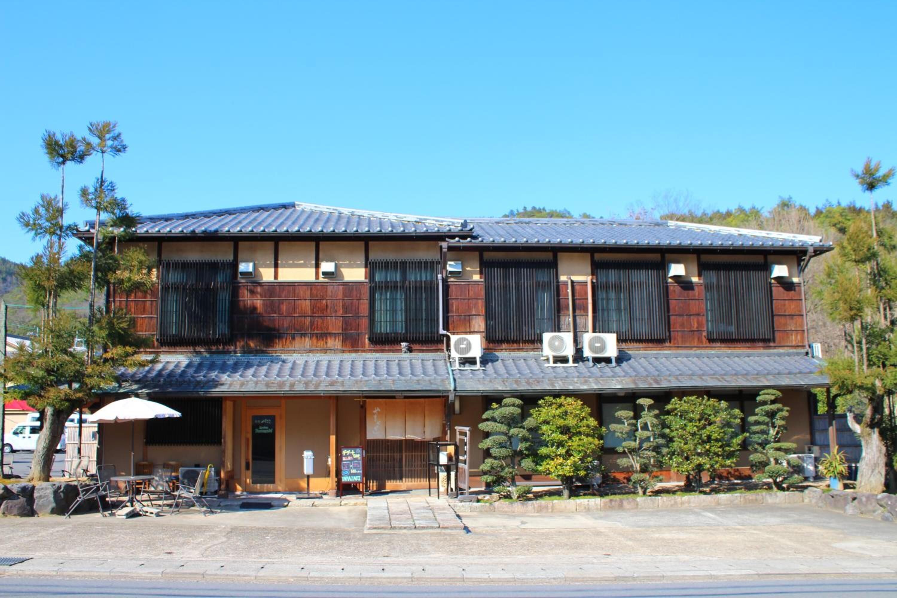 A traditional Japanese building with a two-story structure, wooden exterior, and a covered entrance with a small garden area in front.