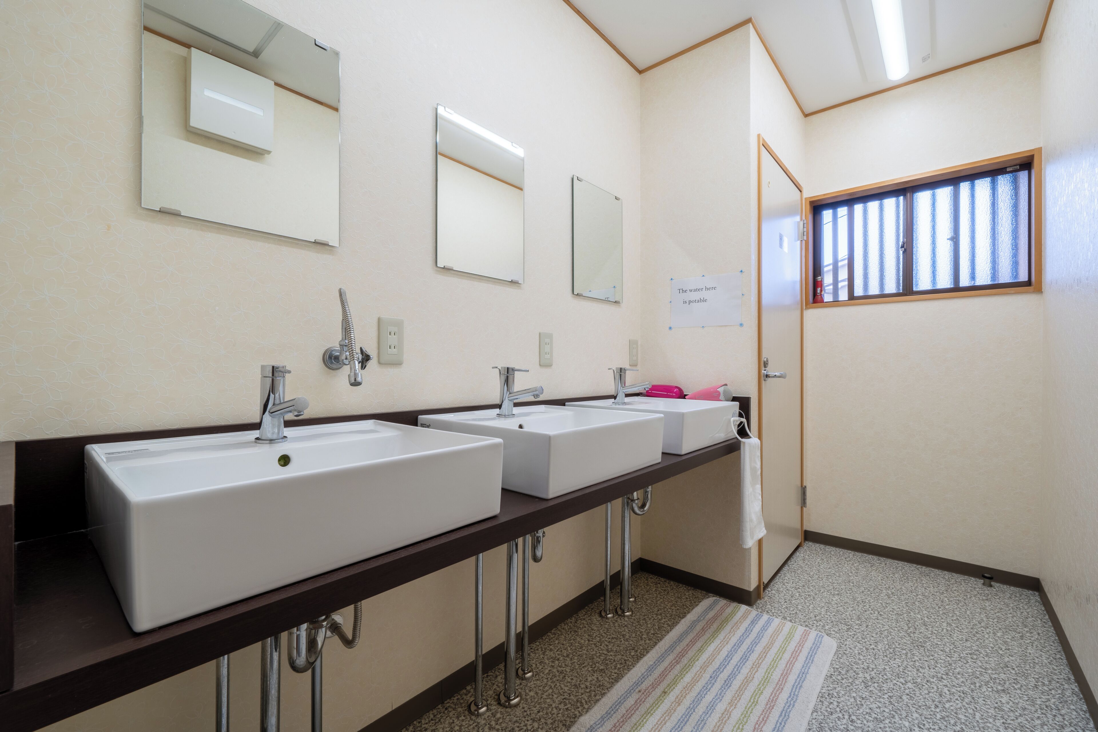 A bathroom with three sinks, a mirror, and a window with bars.