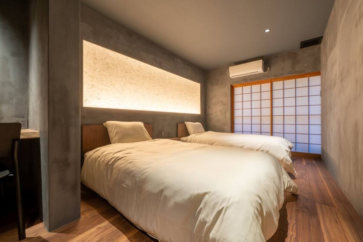 A modern bedroom with two beds, a desk, and a large window with a view.