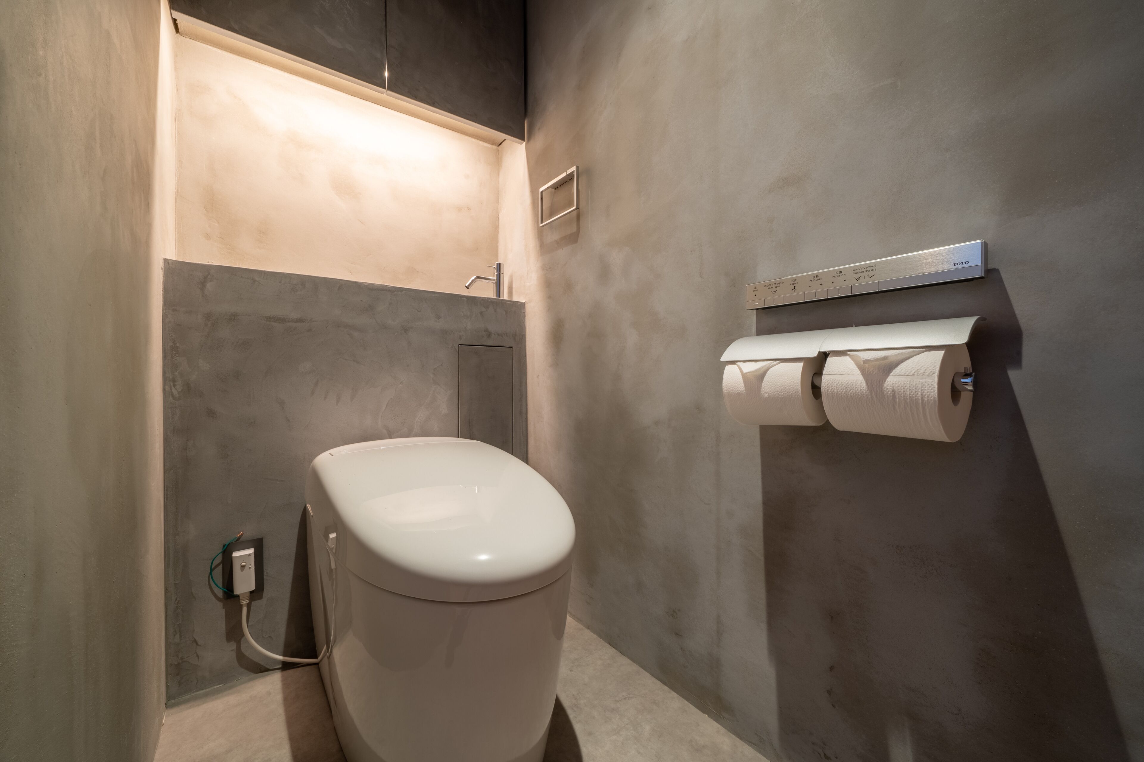 Uma casa de banho moderna com sanita, dispensador de toalhas e suporte de papel higiénico fixado à parede.