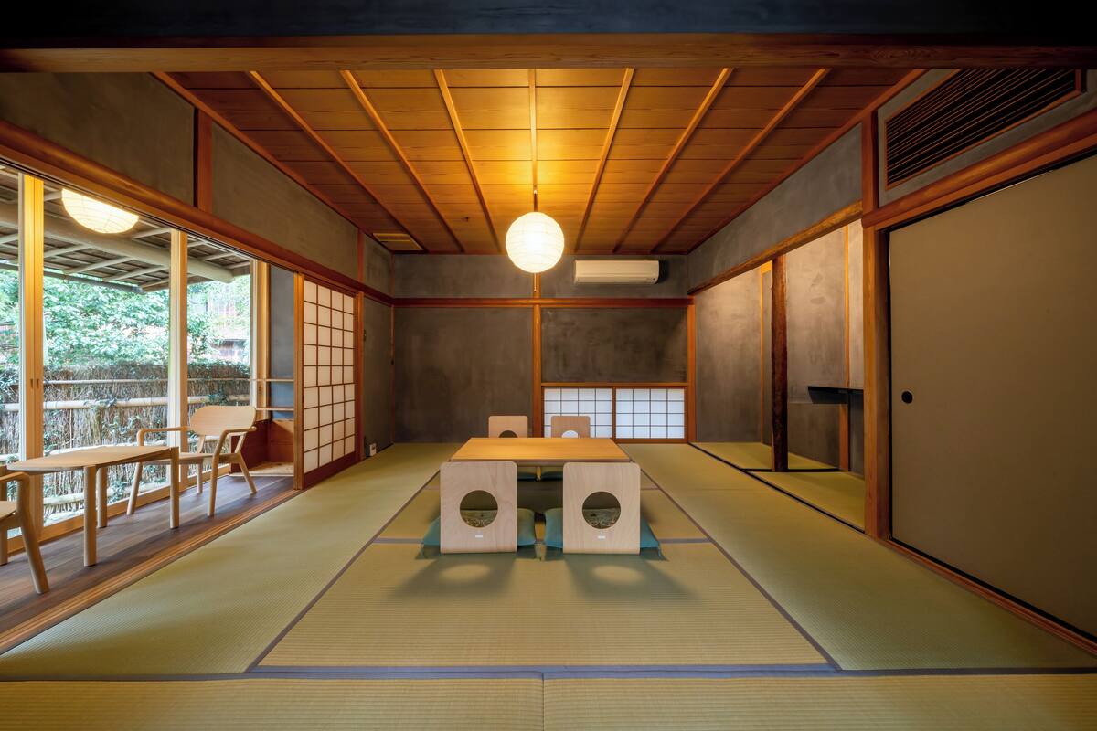 A traditional Japanese room with tatami flooring, a low table with cushions, sliding doors, and a ceiling fan.