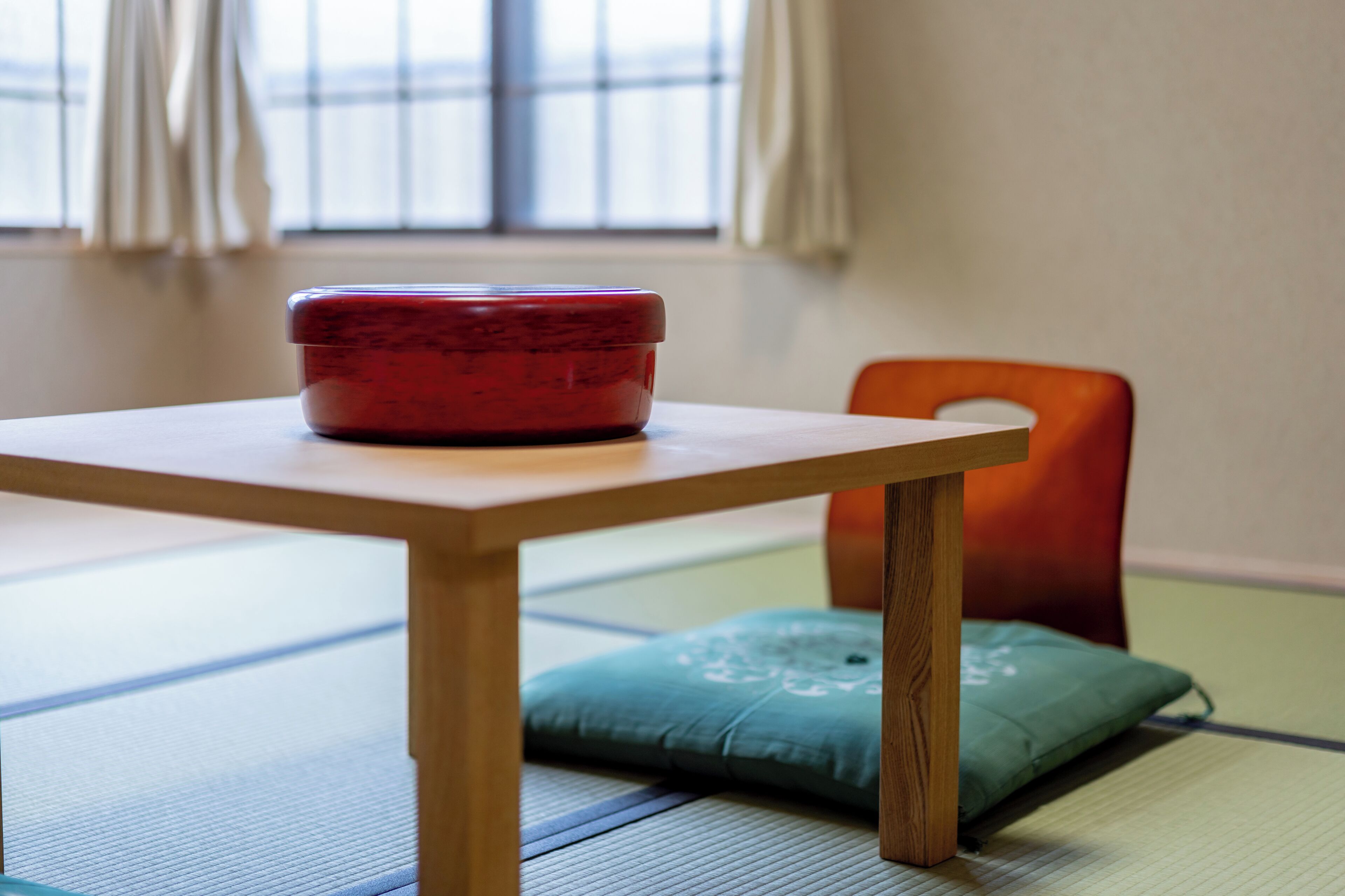 Une pièce avec un sol recouvert de tatamis, une table en bois et un récipient rouge.