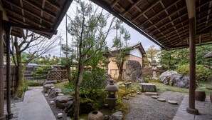 A traditional Japanese garden with stone lanterns, a wooden walkway, and a thatched-roof pavilion.