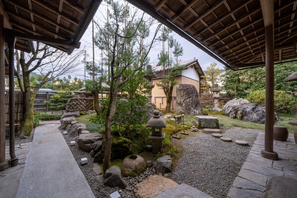 A traditional Japanese garden with stone lanterns, a wooden walkway, and a thatched-roof pavilion. - Ryokan Yamazaki (Kyoto)