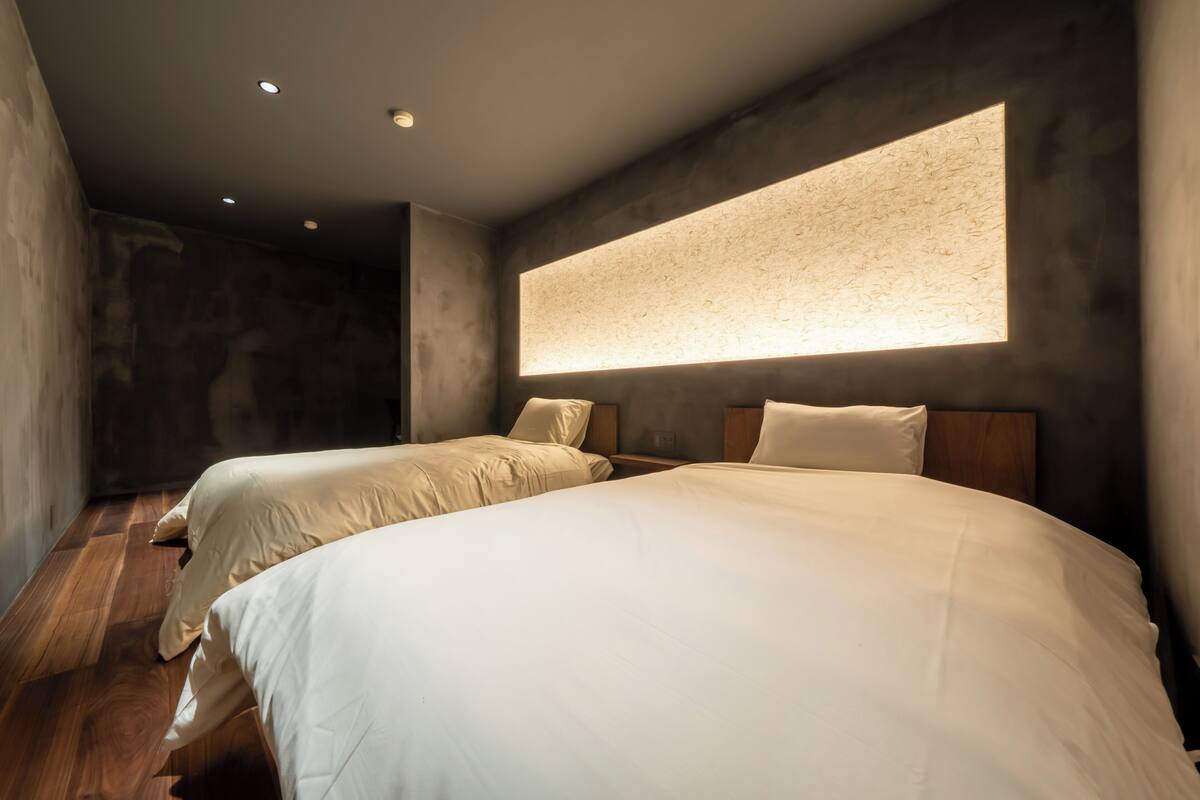 A modern bedroom with two beds, a large window, and a textured wall.