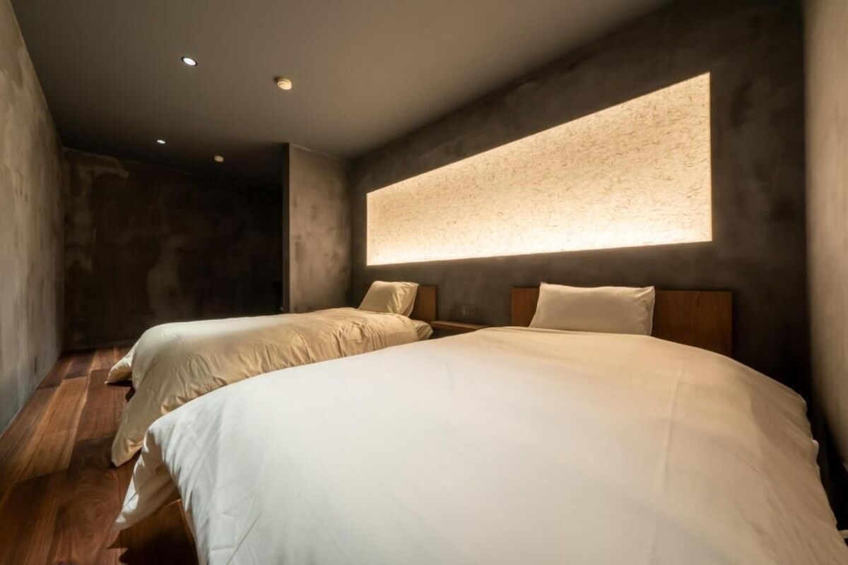 A room with two beds, a large window, and a textured wall.