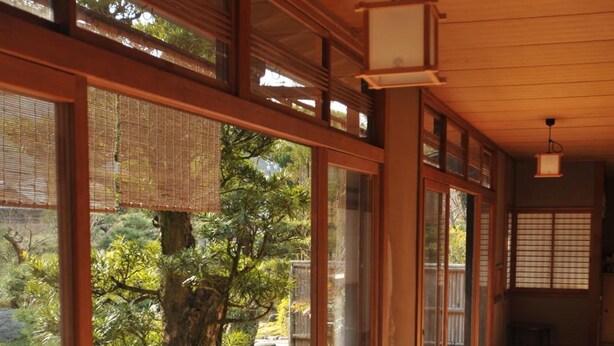 A traditional Japanese interior with sliding doors, a wooden floor, and a view of a garden with a tree and rocks.