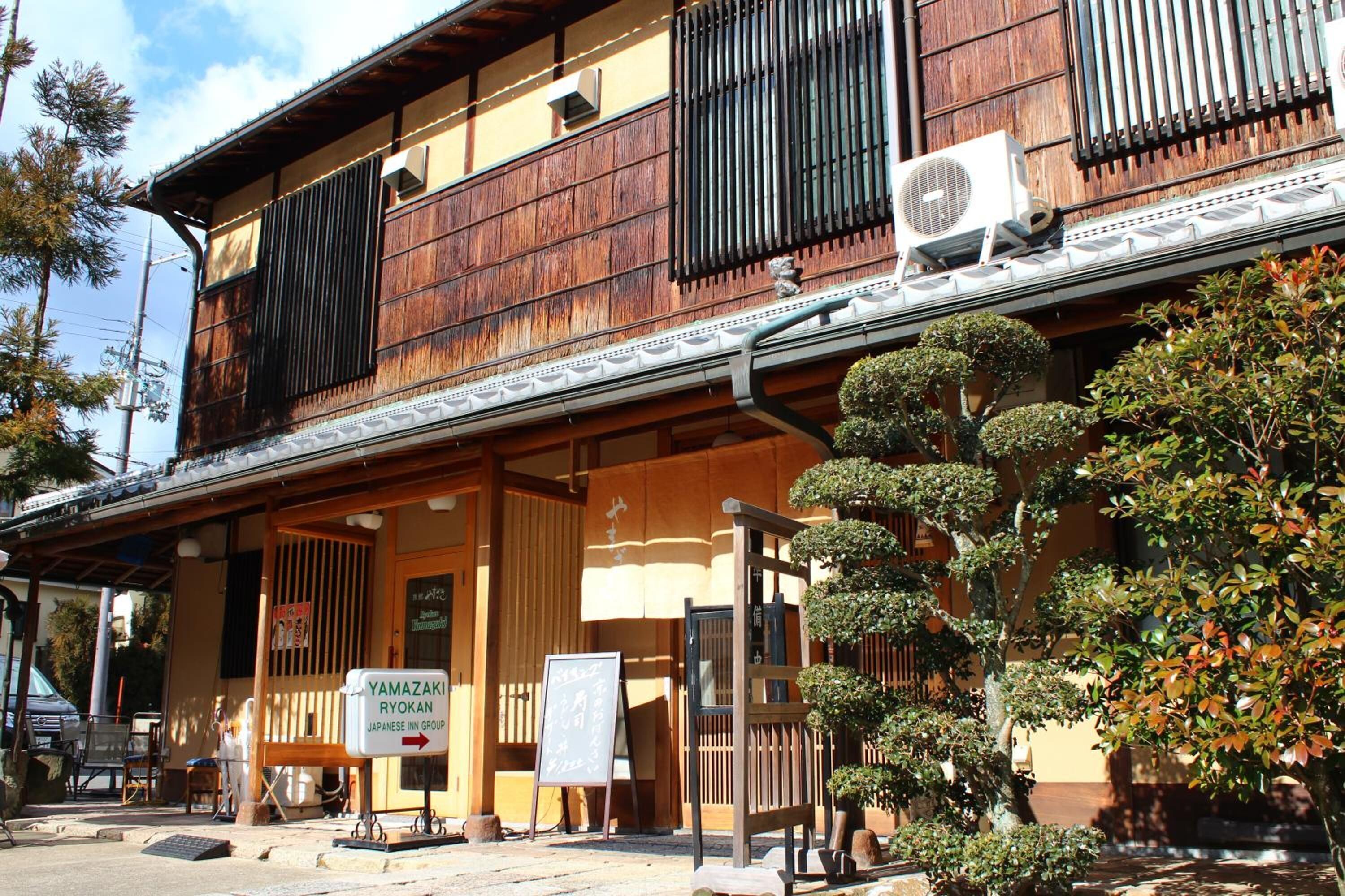 A traditional Japanese ryokan with wooden exterior, tatami mat flooring, and a sign indicating it is part of the Yamazaki Ryokan Japanese Inn Group.