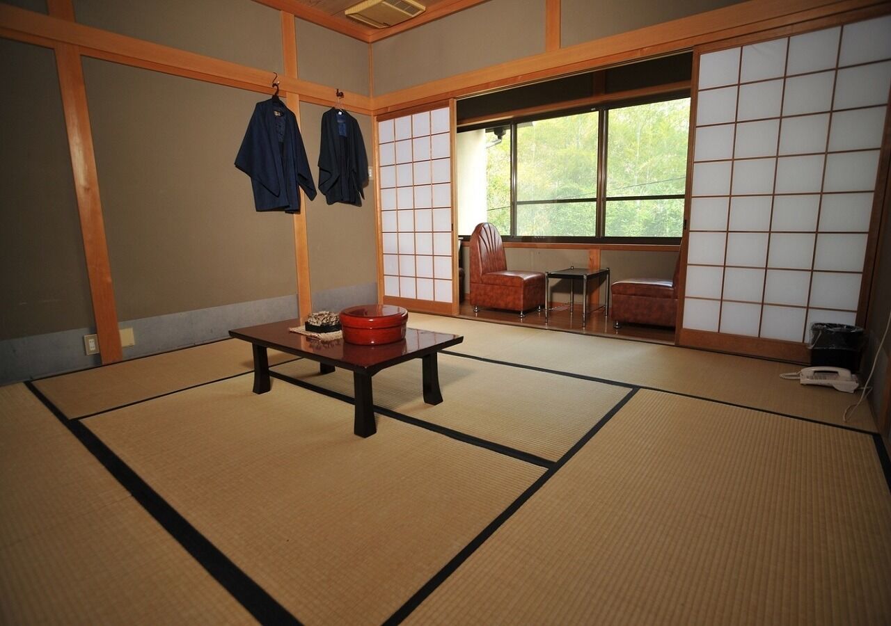 A tatami mat room with a low table, two hanging clothes, a window, and sliding doors.