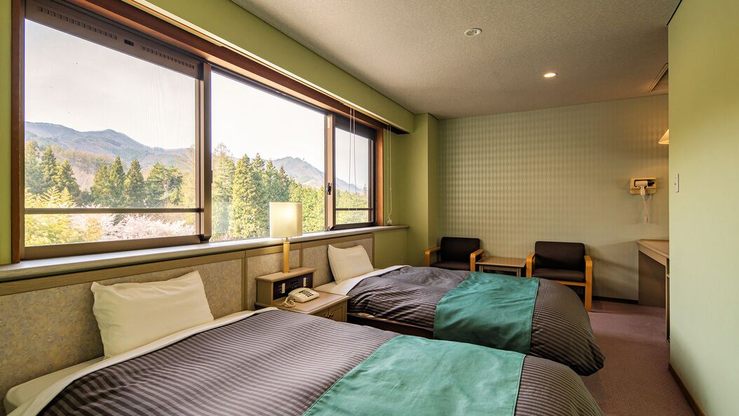 Habitació d'hotel amb dos llits, una taula de treball, una cadira i una finestra que fa vedes a la muntanya.