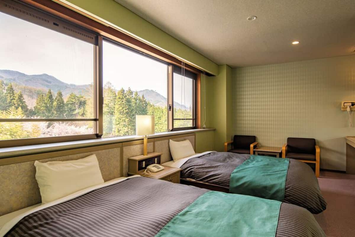 Une chambre d’hôtel avec deux lits, un bureau, une chaise et une fenêtre donnant sur la montagne.
