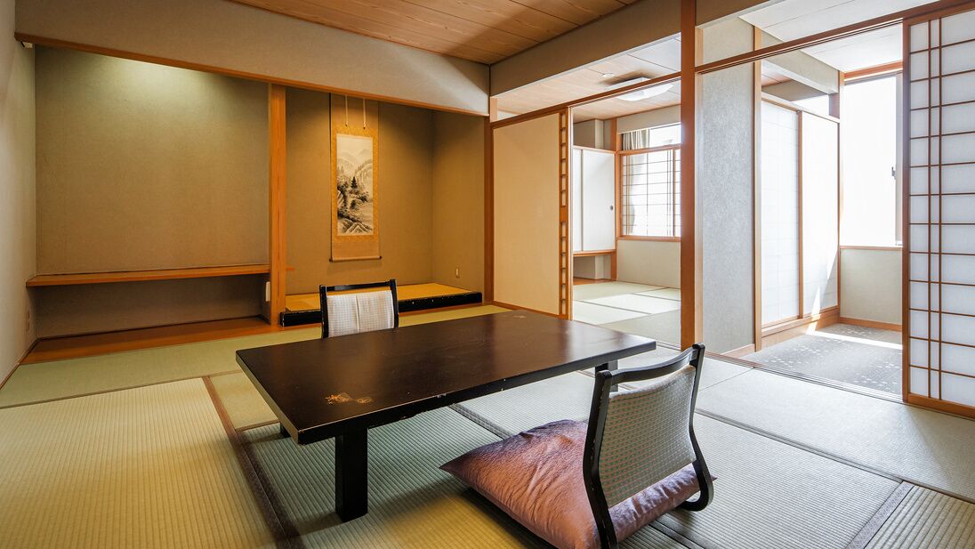 Una habitació japonesa tradicional amb sòls de tatami, una taula baixa, una cadira, portes corredisses i una obra d'art emmarcada a la paret.