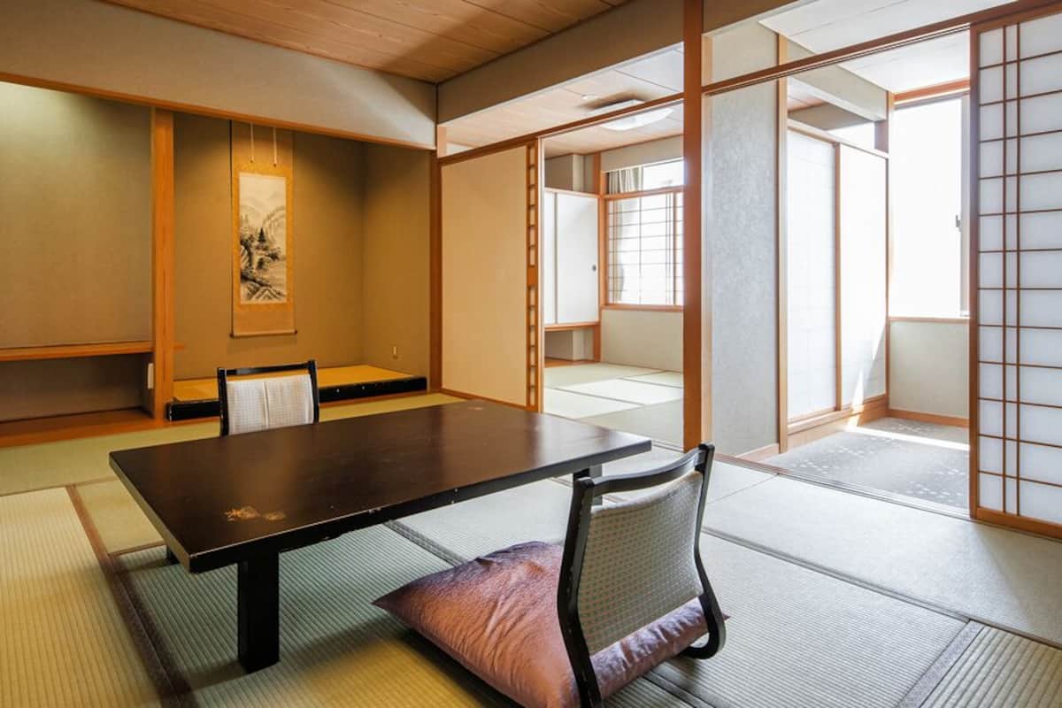 A traditional Japanese room with tatami flooring, a low table, a chair, sliding doors, and a framed artwork on the wall.