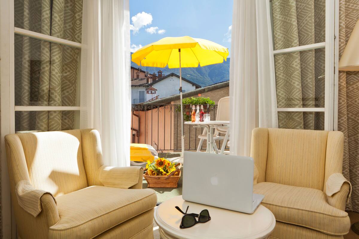 A room with two beige armchairs, a small round table with a laptop and sunglasses, and a yellow umbrella outside.