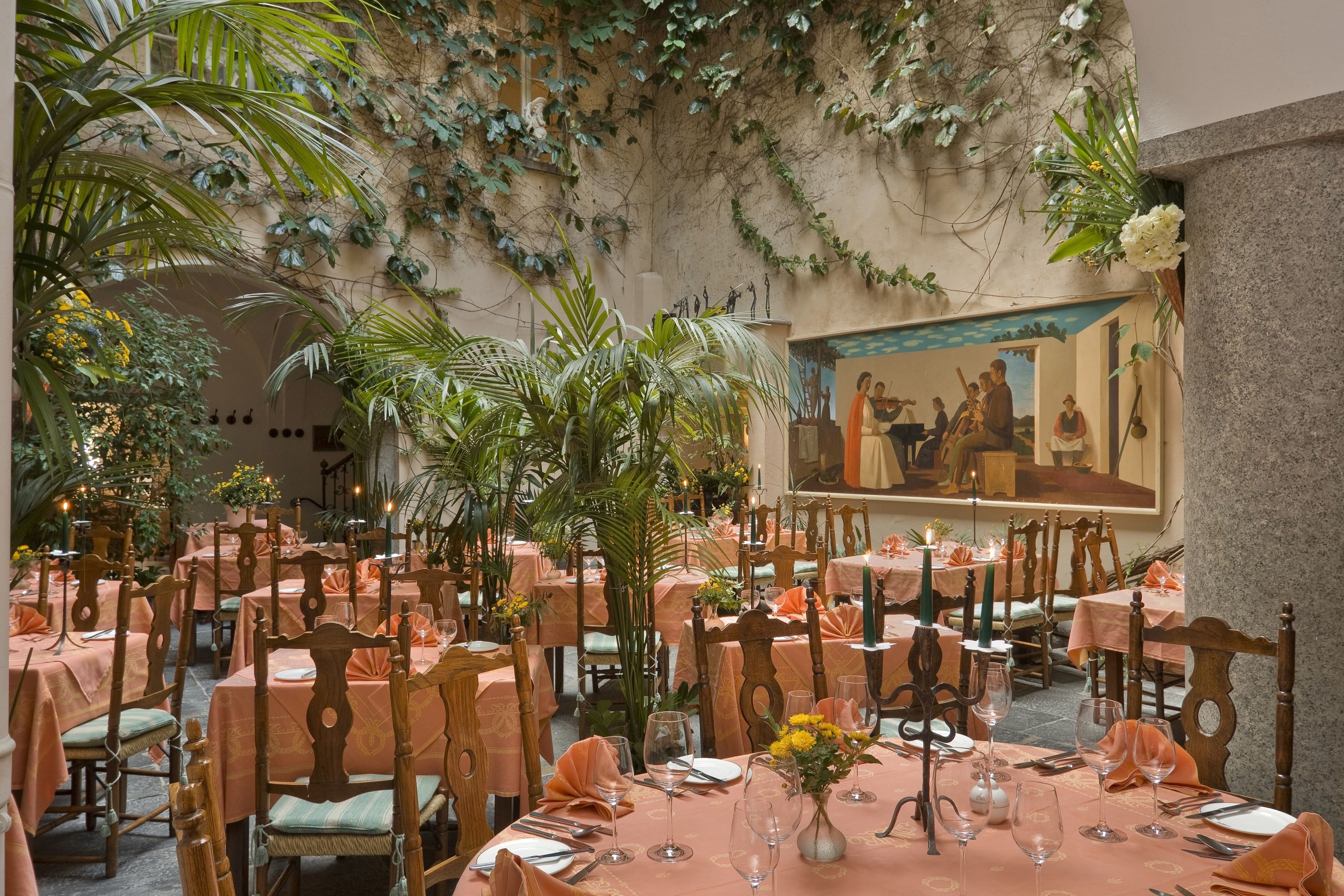 Un restaurante con mesas dispuestas para comer, rodeado de abundante vegetación y un mural en la pared.