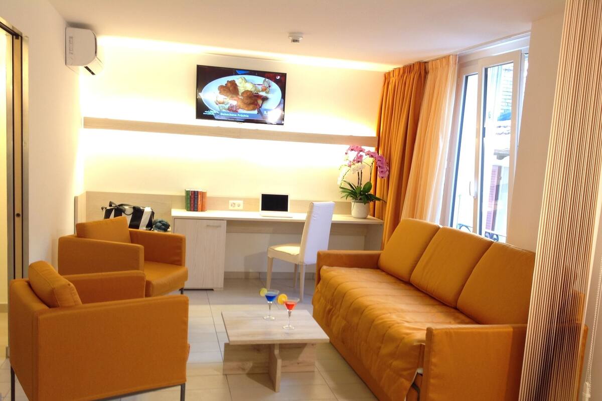 A modern living room with a sofa, armchairs, a coffee table, and a TV mounted on the wall.