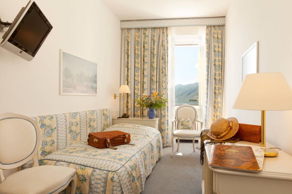 A hotel room with a bed, a chair, a desk, a TV, and a window with curtains.