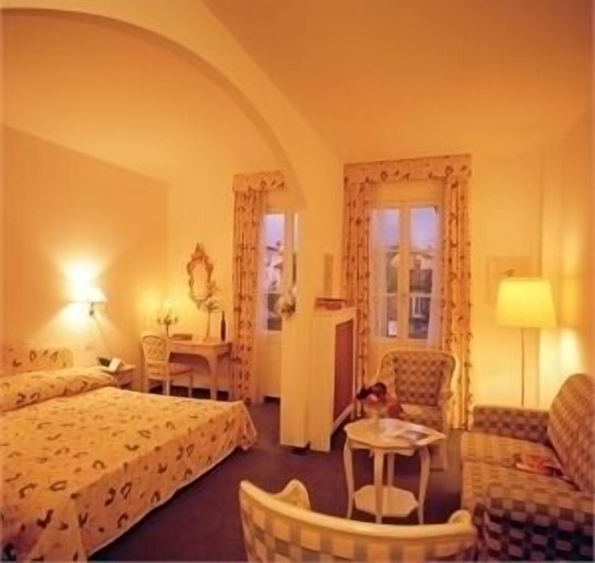 A hotel room with two beds, a desk, a chair, and a small table.