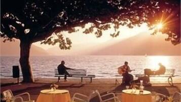 Un restaurante frente al mar con terraza al aire libre bajo un árbol.