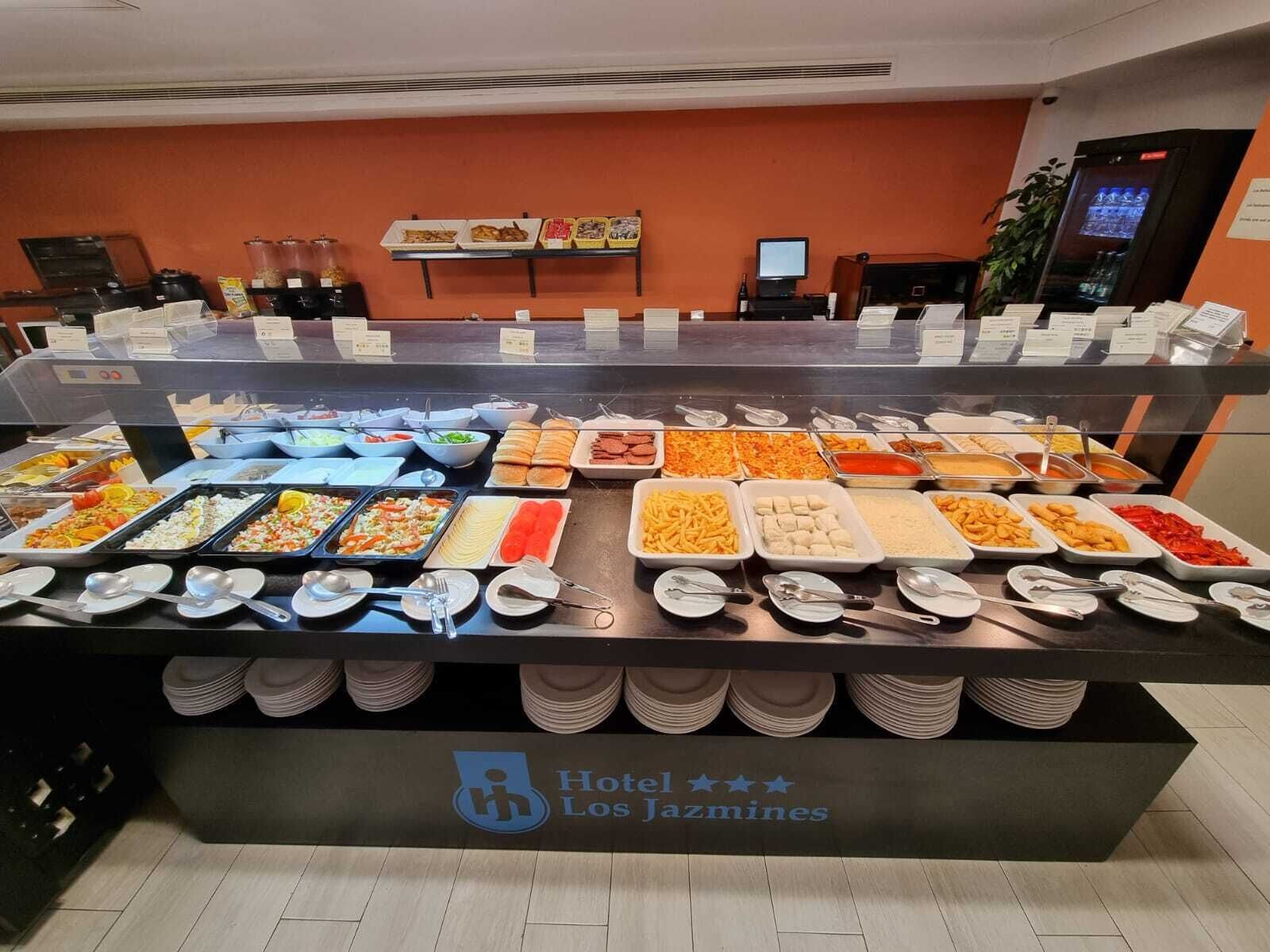 A buffet counter with various food options and a sign indicating Hotel Los Jazmines.