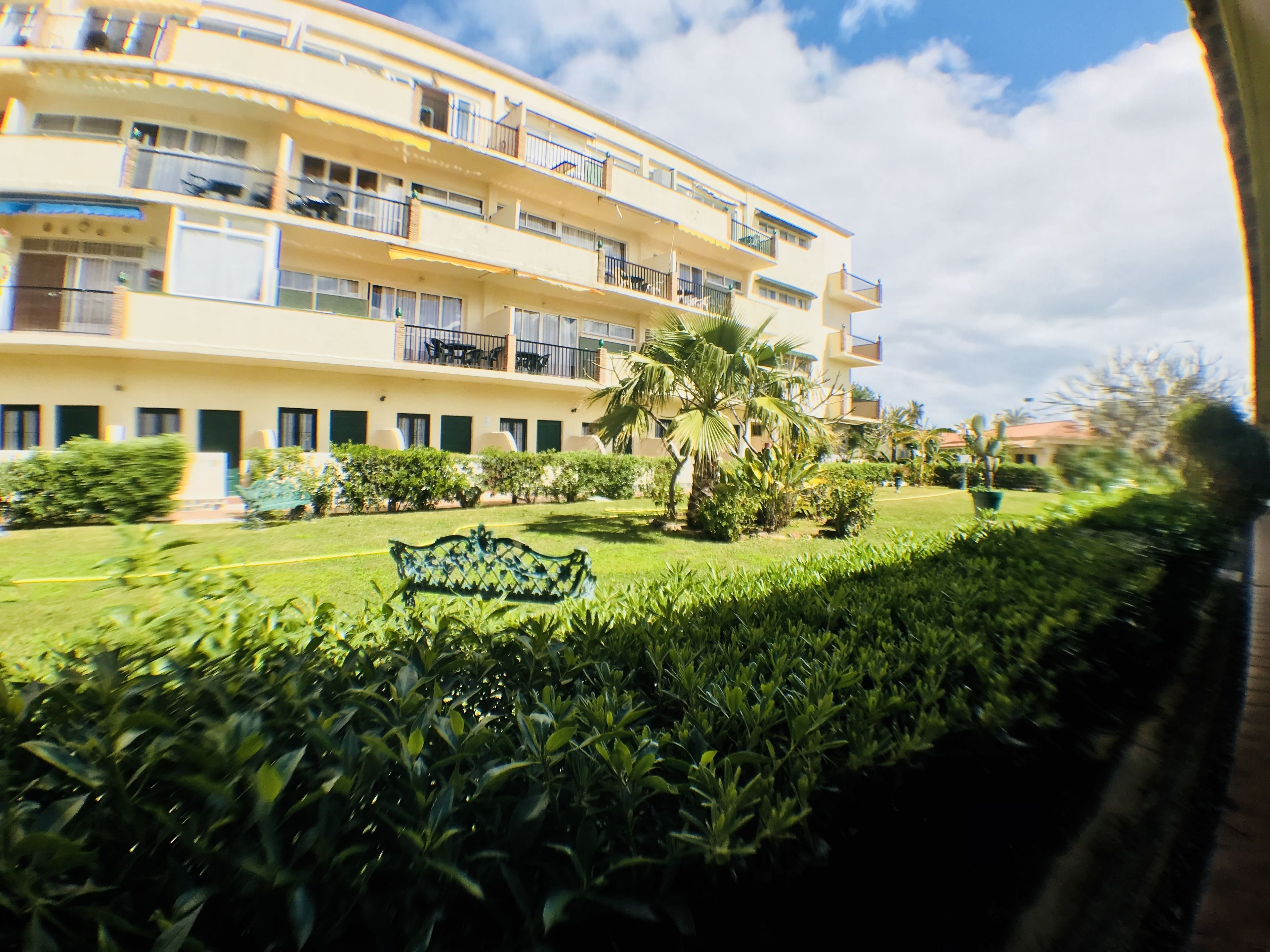 A multi-story building with balconies, a well-maintained lawn, and a bench.