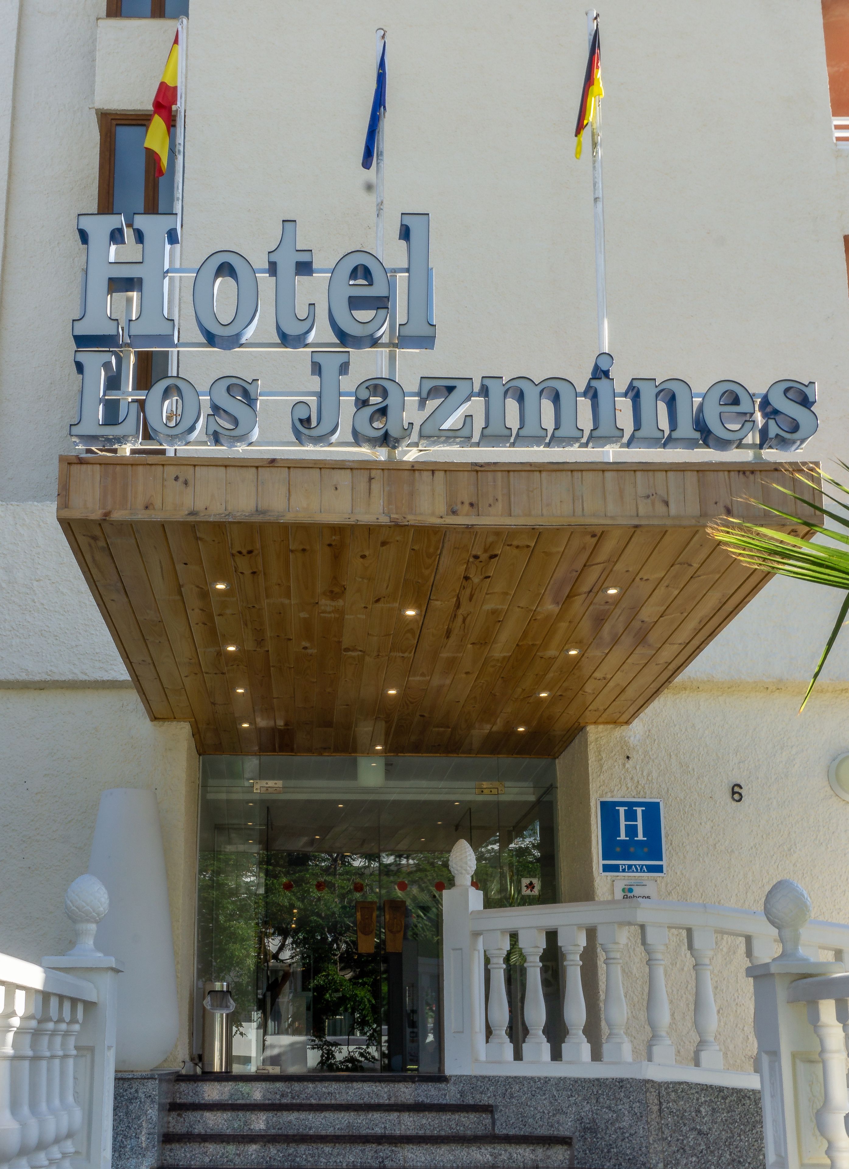 L’entrée d’un hôtel, avec un auvent en bois et une enseigne indiquant « Hôtel Los Jazmines ».