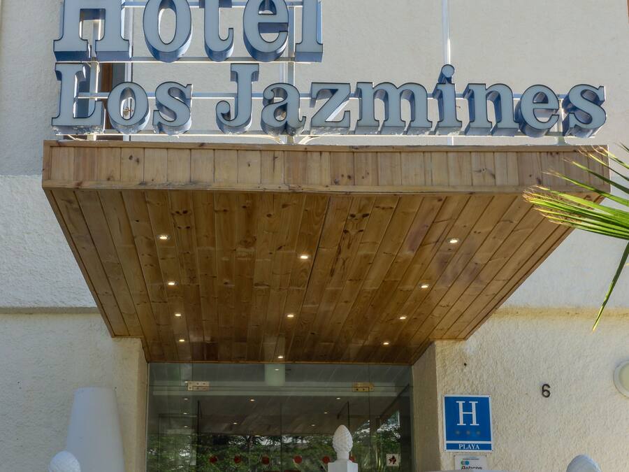 L’entrée d’un hôtel, avec un auvent en bois et une enseigne indiquant « Hôtel Los Jazmines ».