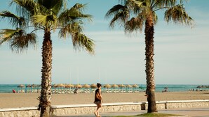 A beach scene with palm trees, a stone wall, and beach umbrellas. - Hotel Los Jazmines (Torremolinos)