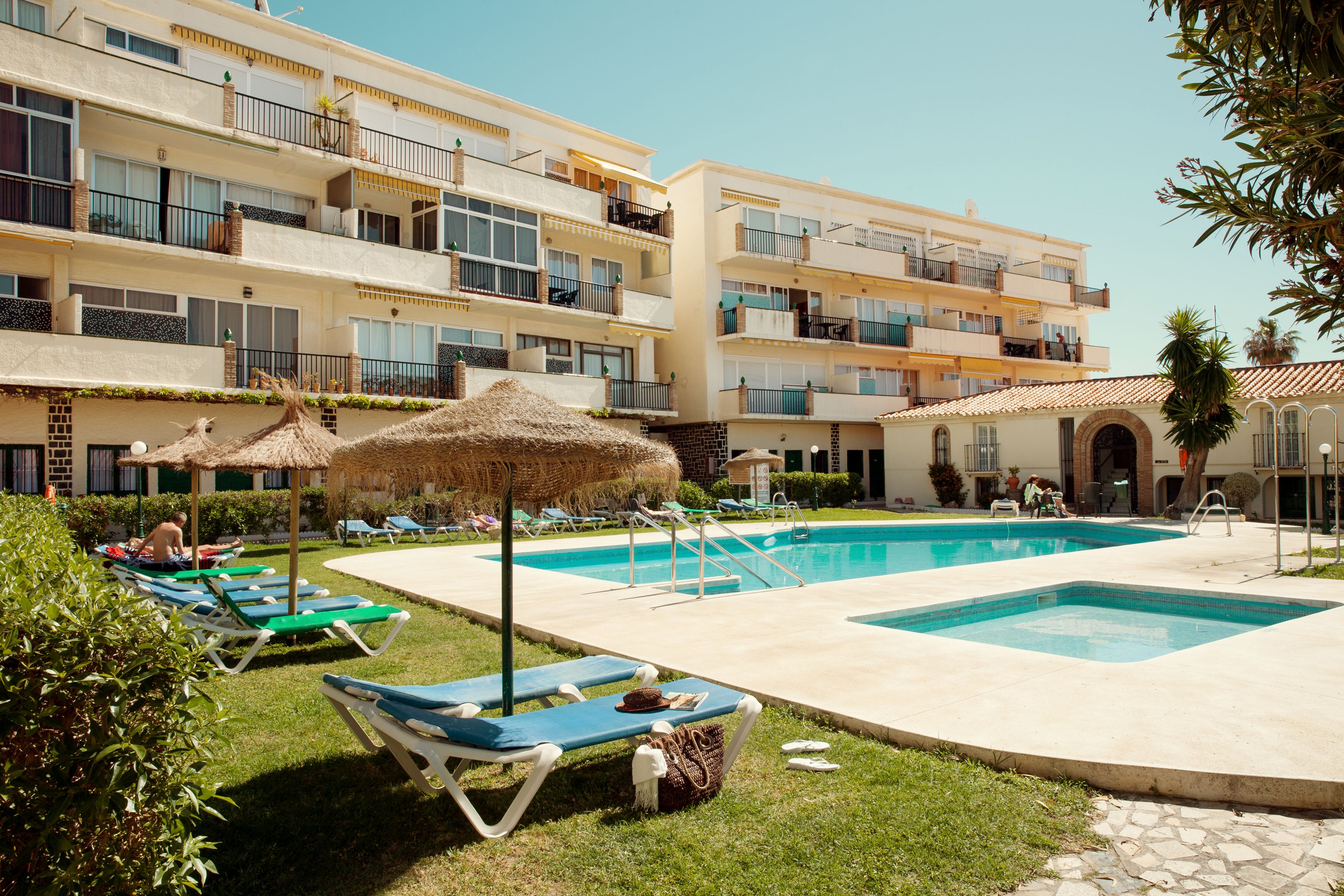 Zona de piscina de un hotel con sillones, alberca y un edificio con balcones.