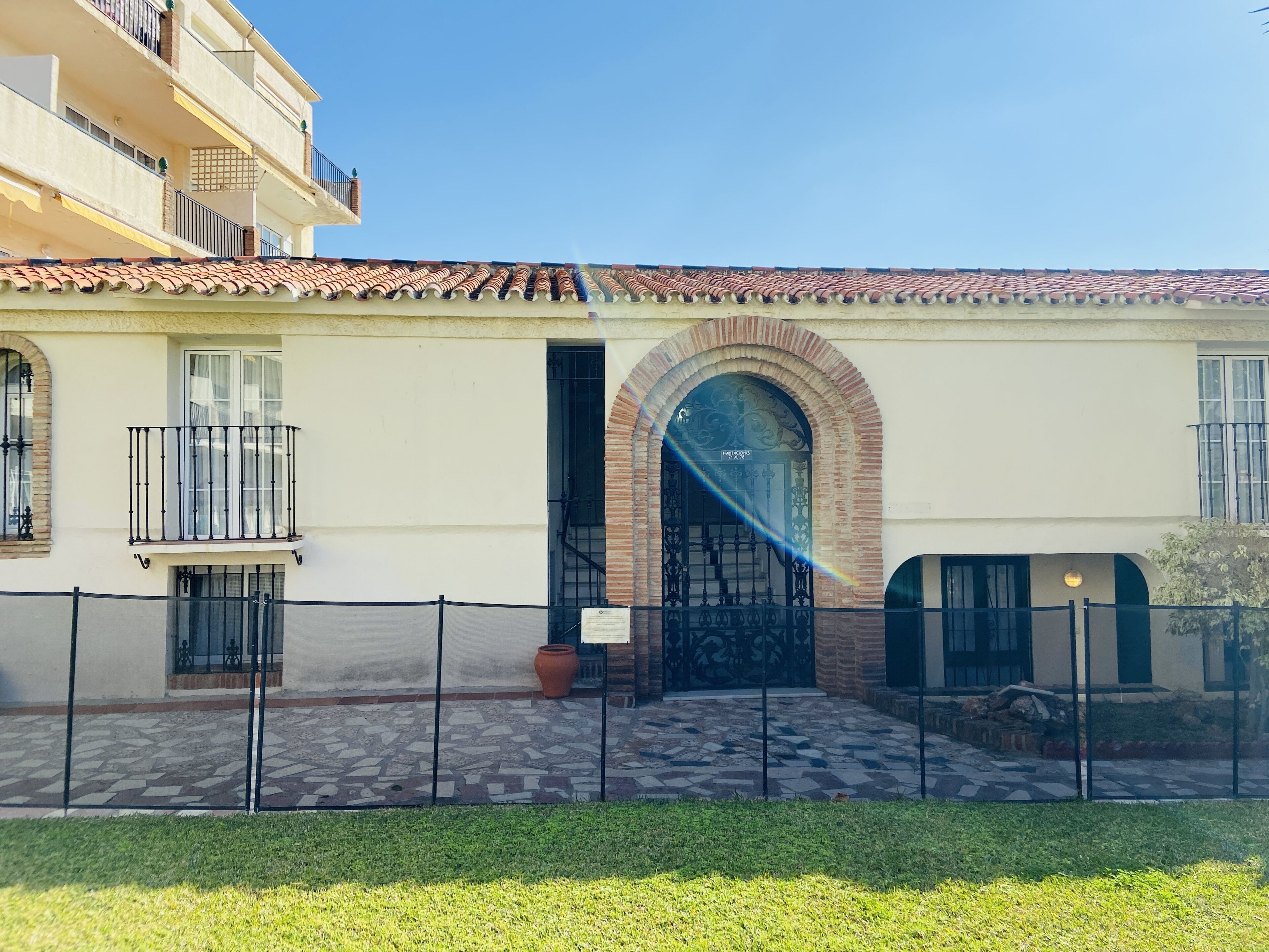 A building with a tiled roof, a central arched entrance, and a balcony with a metal railing.