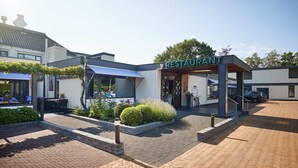 A restaurant with a covered outdoor seating area, a brick pathway, and a modern building facade.