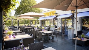 An outdoor patio area with tables and chairs, umbrellas, and potted plants.