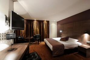 A modern hotel room with a flat-screen TV, a desk with a lamp, a leather chair, a bed with a brown blanket, and a wooden headboard. - Van der Valk Hotel Hardegarijp - Leeuwarden (Hurdegaryp)