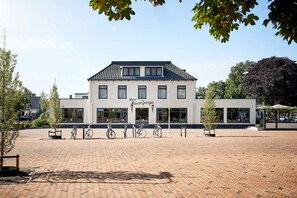 A building with a tiled roof and multiple windows, surrounded by a paved area with bicycles parked in front. - Van der Valk Hotel Hardegarijp - Leeuwarden (Hurdegaryp)