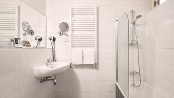 Een moderne badkamer met een witte wastafel, twee spiegels, een handdoekrek en een douche met glazen wanden.