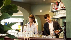 A bar area with two staff members, shelves with bottles and glasses, and a bar counter.