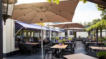 Een terras buiten met meerdere tafels en stoelen, parasols en potplanten.