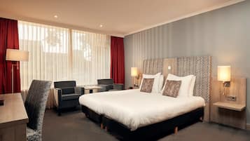 A hotel room with a large bed, a desk, a chair, and a nightstand with a lamp.