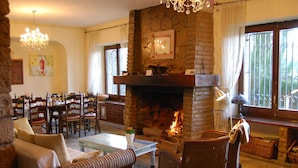 A cozy living room with wicker furniture, a stone fireplace, and a dining area with wooden chairs and tables. - Arianella B&B Penedes (Torrelles de Foix)