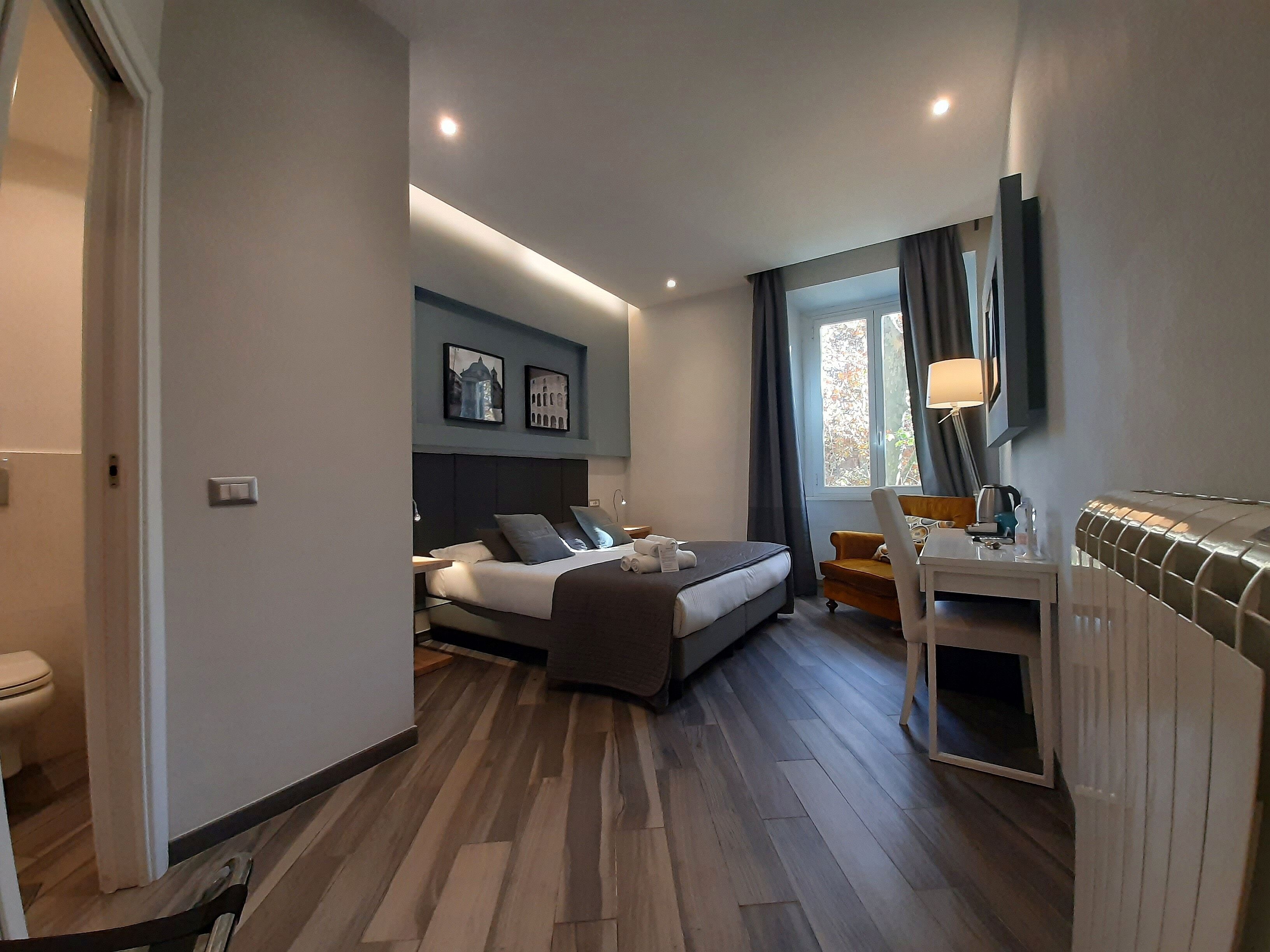 A modern hotel room with a bed, bedside table, lamp, and a view of the outdoors.