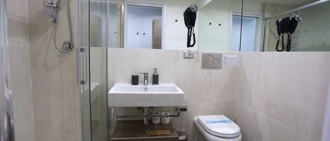 Baño pequeño con ducha de vidrio, lavamanos blanco con espejo arriba y un inodoro con un adhesivo azul.