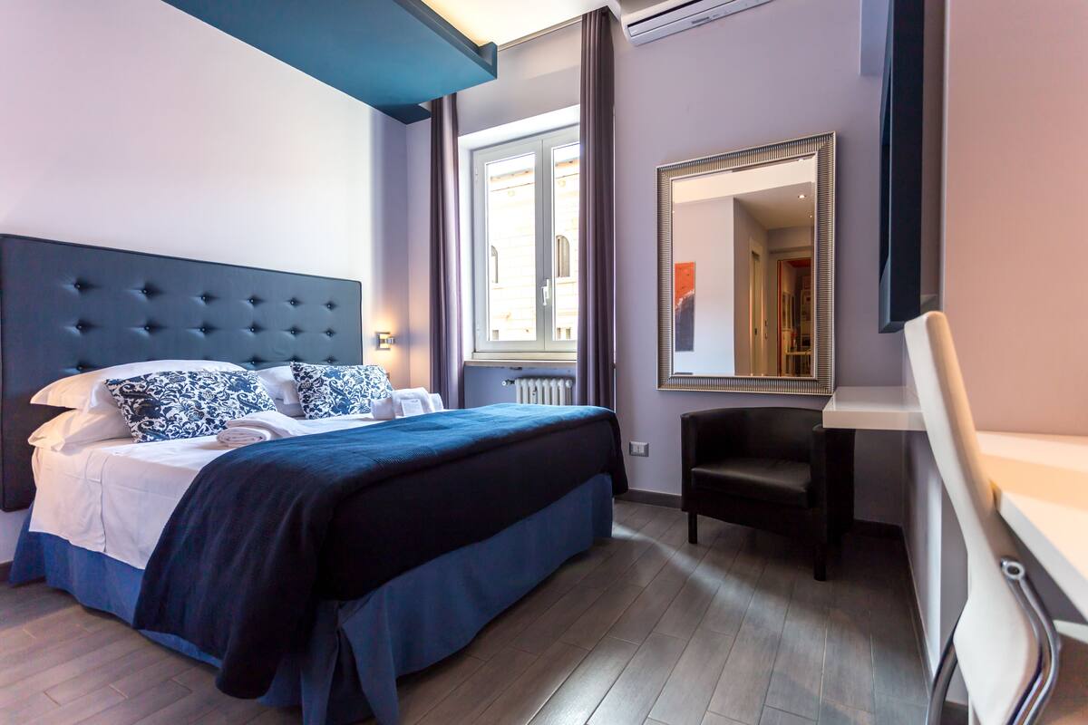 A modern hotel room with a large bed, a desk, and a mirror.