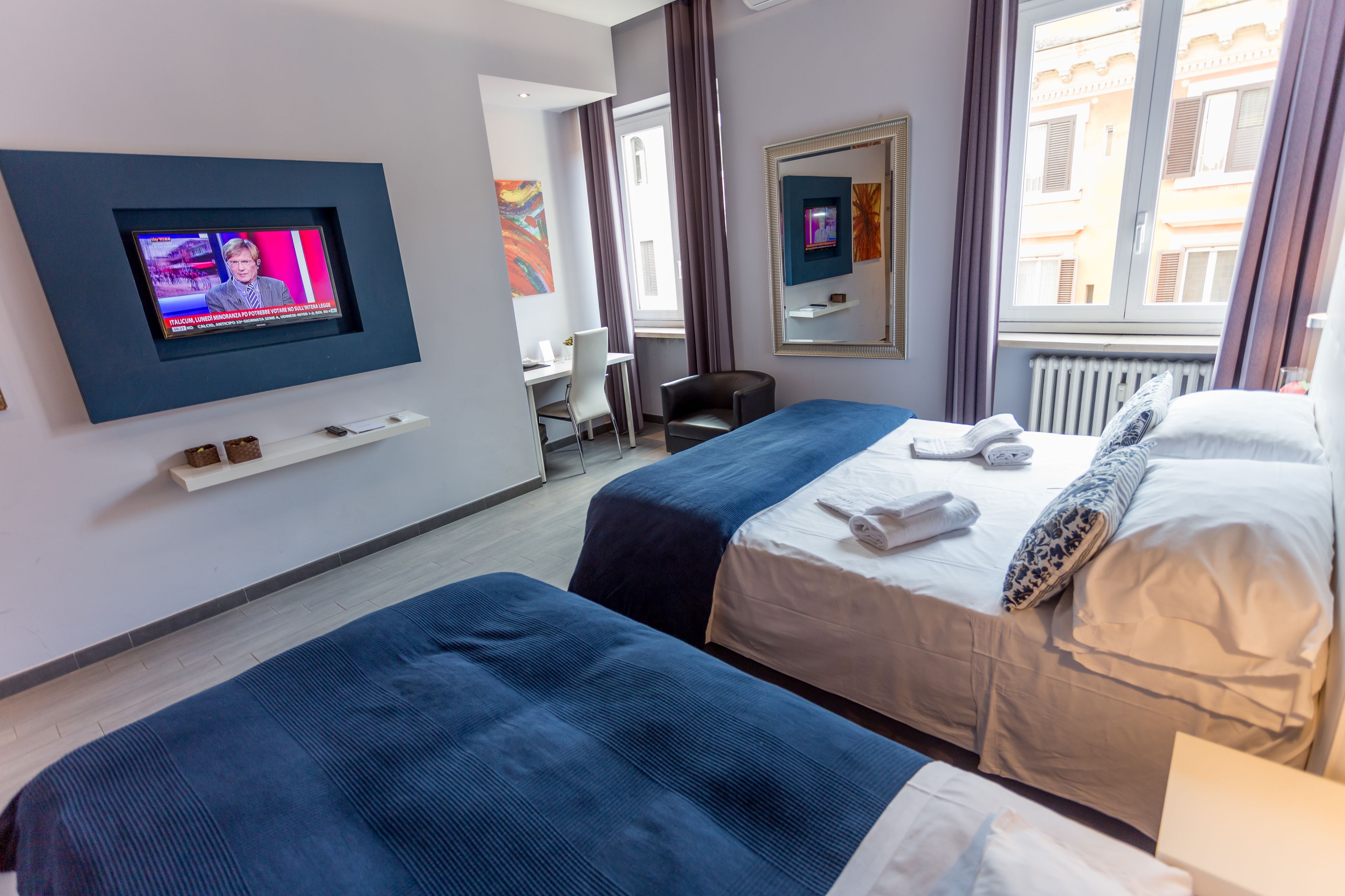 Een hotelkamer met twee bedden, een aan de muur bevestigde televisie, een bureau en een stoel.