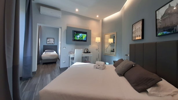 A hotel room with a large bed, a desk, a chair, a TV, a mirror, and a window. - B&B Home 77 (Rome)