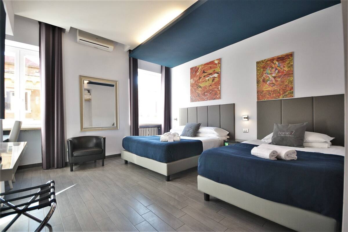 A hotel room with two beds, a desk, a chair, and artwork on the walls.