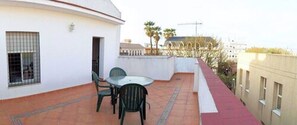 A rooftop terrace with a table and chairs, a small door, and a view of buildings and palm trees. - Apartamentos Sevilla (Seville)