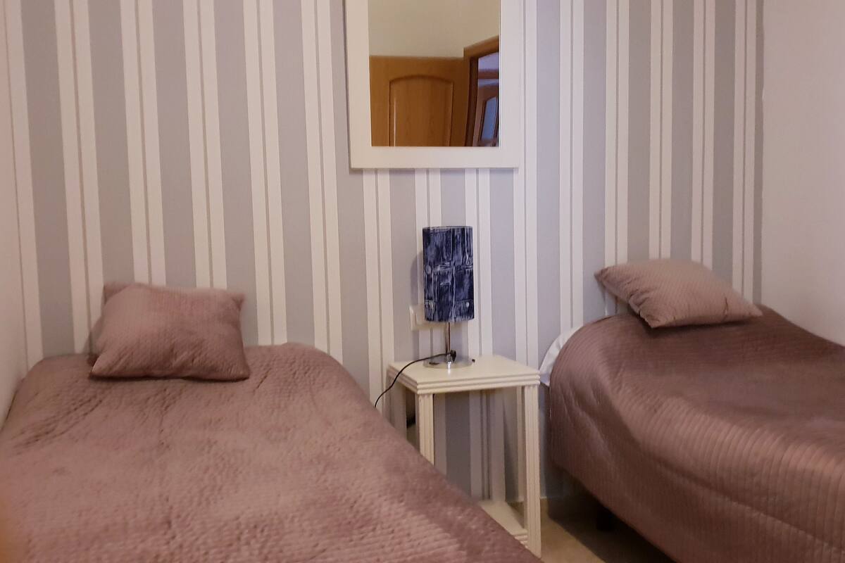 Una habitación con dos camas, una mesita con una lámpara y un espejo en la pared.