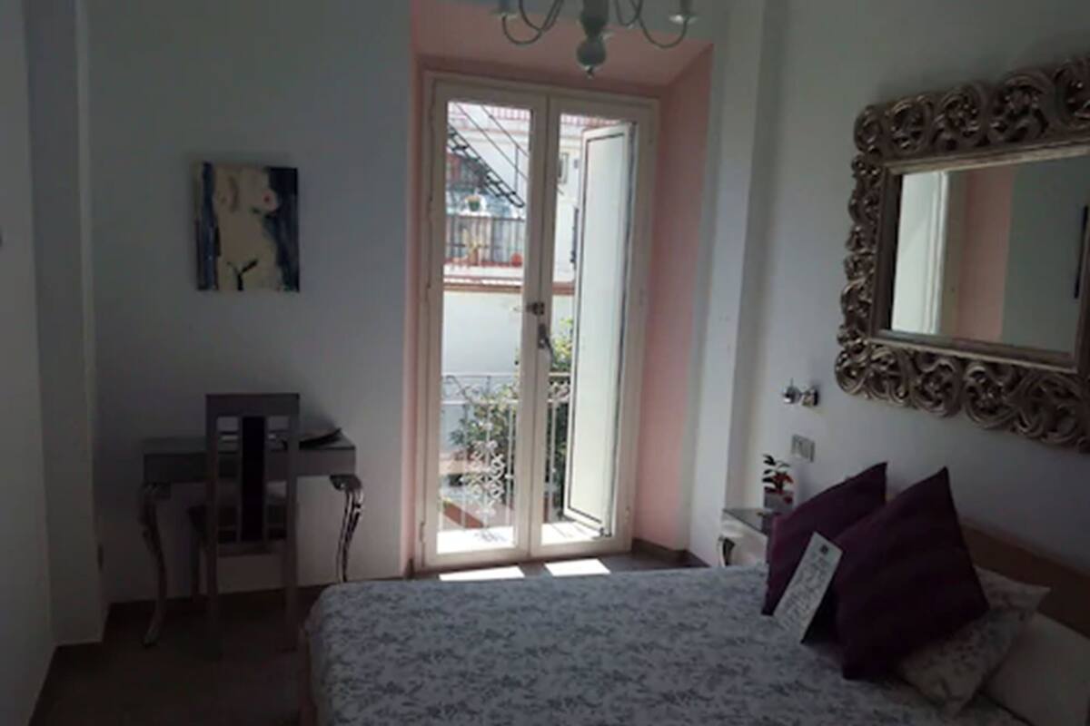 A bedroom with a bed, a desk, a chair, a door leading to a balcony, and a large mirror on the wall.