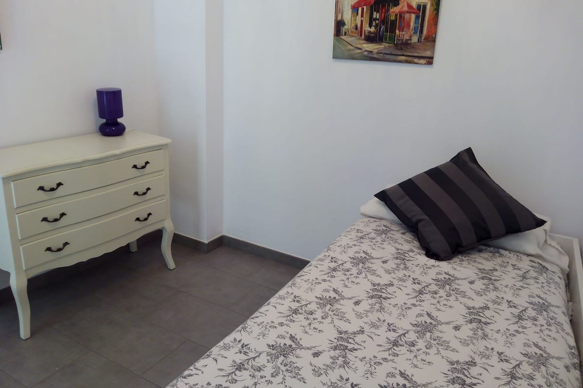 A bedroom with a bed, a nightstand, a dresser, and a painting on the wall.